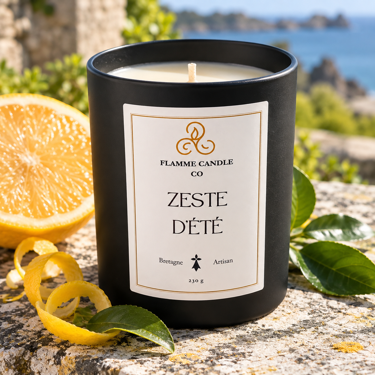 Bougie Zeste d'Été sur un rocher, avec une tranche d'orange, un zeste de citron et des feuilles vertes, mer au loin