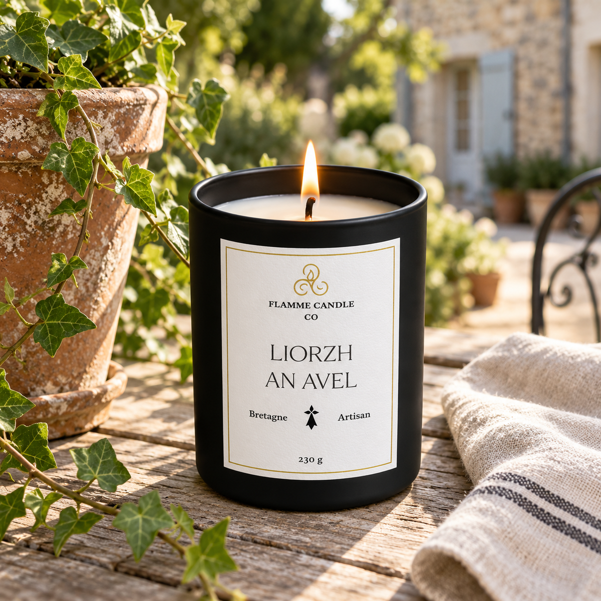 Bougie Liorzh an Avel allumée sur une table de jardin près d'un pot en terre cuite, avec du lierre et un torchon rayé