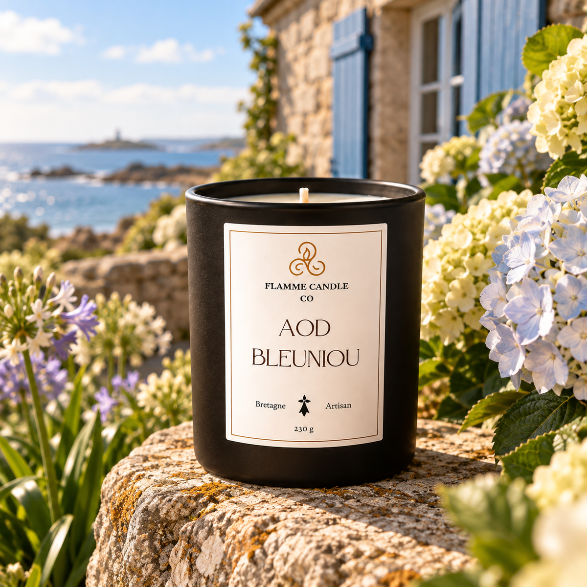 Bougie Aod Bleuniou posée sur un rocher devant des hortensias et des fleurs sauvages, mer au loin